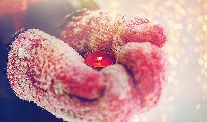 Image showing close up of hands in winter mittens holding candle