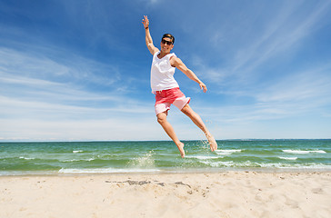 Image showing smiling young man jumping on summer beach