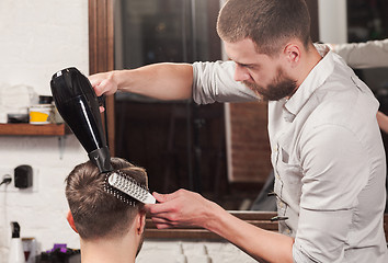 Image showing Young handsome barber making haircut of attractive man in barbershop