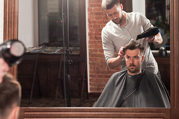 Image showing Young handsome barber making haircut of attractive man in barbershop