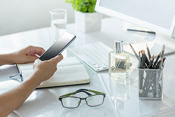 Image showing Close-up of female hands using smart phone while working on computer at modern office interior