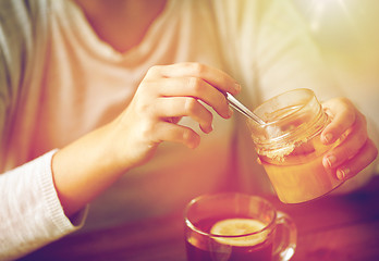 Image showing close up of woman adding honey to tea with lemon