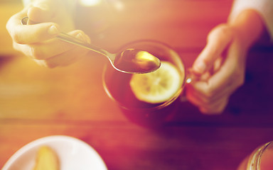 Image showing close up of woman adding honey to tea with lemon