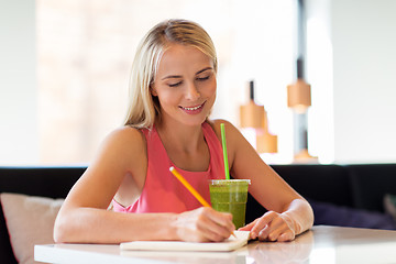 Image showing woman with drink writing to notebook at restaurant