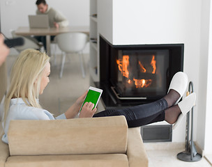 Image showing young woman using tablet computer in front of fireplace