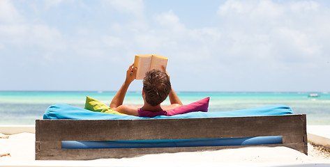 Image showing Relaxed man reading book in luxury lounger enjoying summer vacations on beautiful beach.