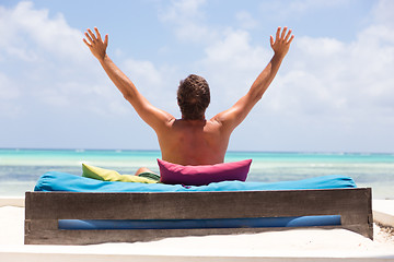 Image showing Relaxed man in luxury lounger, arms rised, enjoying summer vacations on beautiful beach.