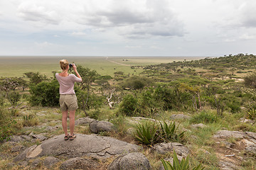 Image showing Female tourist looking through binoculars on African safari in Serengeti national park. Tanzania, Afrika.