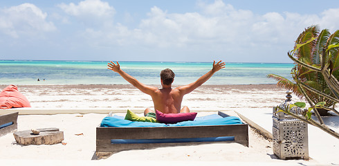 Image showing Relaxed man in luxury lounger, arms rised, enjoying summer vacations on beautiful beach.