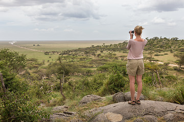 Image showing Female tourist looking through binoculars on African safari in Serengeti national park. Tanzania, Afrika.