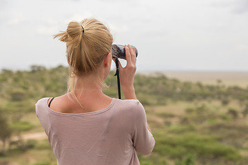 Image showing Female tourist looking through binoculars on African safari in Serengeti national park. Tanzania, Afrika.