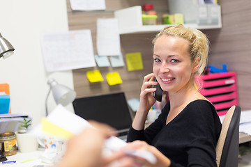 Image showing Business woman talking on mobile phone accepting papers.