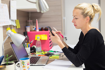 Image showing Female entrepreneur texting on mobile phone in colorful modern creative working environment.