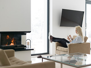 Image showing young woman using tablet computer in front of fireplace