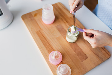 Image showing hands with jar and scoop making formula milk