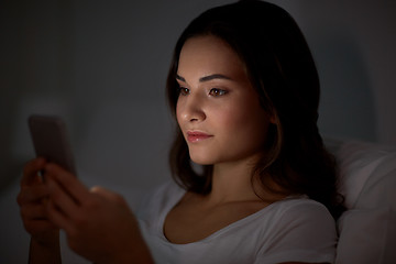 Image showing happy young woman with smartphone in bed at night