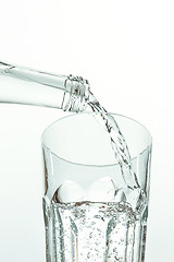 Image showing Pouring water from bottle into glass on white