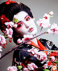 Image showing young pretty geisha in kimono with sakura and red decoration des