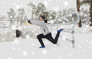 Image showing sports man stretching leg at fence in winter