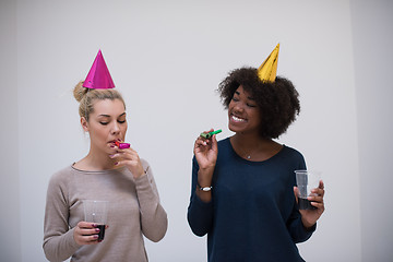 Image showing smiling women in party caps blowing to whistles