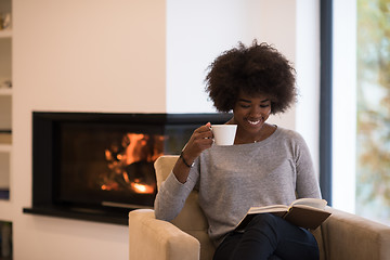 Image showing black woman reading book  in front of fireplace