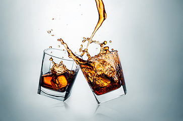 Image showing Two whiskey glasses clinking together on gray