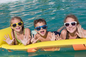 Image showing Three happy children playing on the swimming pool at the day tim