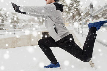 Image showing sports man stretching leg at fence in winter