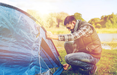 Image showing happy male traveler setting tent up outdoors