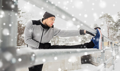 Image showing sports man stretching leg at fence in winter