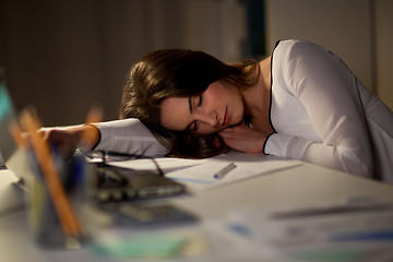 Image showing tired woman sleeping on office table at night