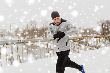 Image showing man with earphones running along winter bridge