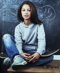 Image showing young cute teenage girl in classroom at blackboard seating on ta