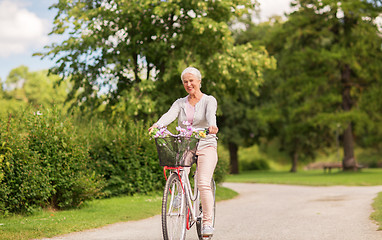 Image showing happy senior woman riding bicycle at summer park