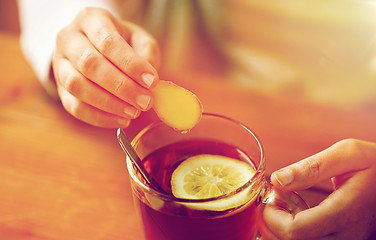 Image showing close up of woman adding ginger to tea with lemon