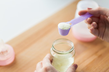 Image showing hands with jar and scoop making formula milk