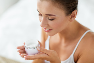 Image showing close up of happy woman holding and smelling cream