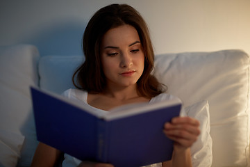 Image showing young woman reading book in bed at night home