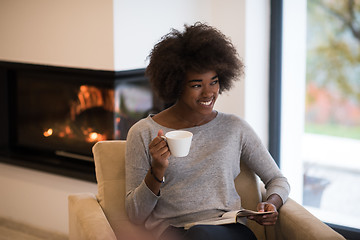 Image showing black woman reading book  in front of fireplace