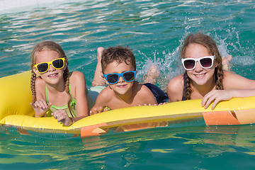 Image showing Three happy children playing on the swimming pool at the day tim