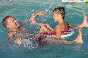 Image showing Father and son  playing in the swimming pool at the day time.