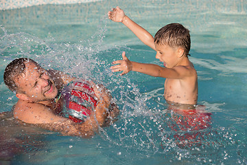 Image showing Father and son  playing in the swimming pool at the day time.