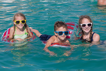 Image showing Three happy children playing on the swimming pool at the day tim