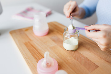 Image showing hands with jar and scoop making formula milk