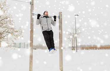 Image showing young man exercising on horizontal bar in winter