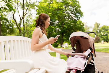 Image showing happy mother with smartphone and stroller at park