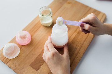 Image showing hands with bottle and scoop making formula milk