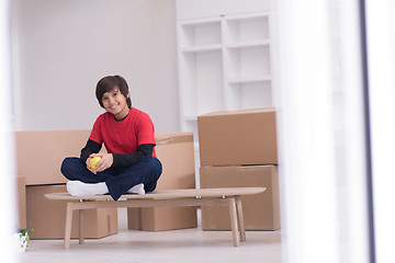 Image showing boy sitting on the table with cardboard boxes around him