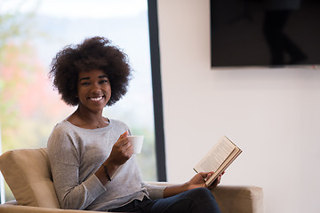 Image showing black woman reading book  in front of fireplace