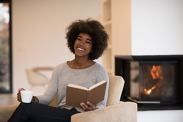 Image showing black woman reading book  in front of fireplace